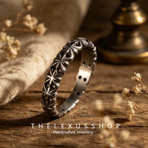 May include: A silver-toned metal ring featuring a repeating star-like geometric pattern around the exterior band. The ring has a dark, oxidized finish within the recessed areas of the design. The text THELEXUSSHOP Handcrafted Jewellery is visible.