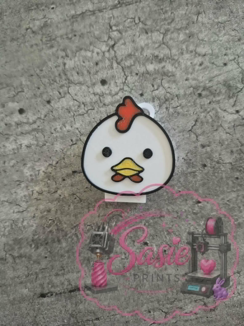 May include: A white chicken-shaped charm with a red comb, black eyes, and a yellow beak. The charm features a black outline and a small white loop at the top for attachment. A pink watermark with the text Sasie PRINTS is visible at the bottom.