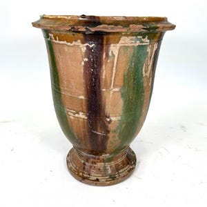 May include: A tall, flared ceramic vessel featuring a glazed finish with vertical streaks of dark brown, forest green, and tan. The pot has a wide, flat rim, a tapered body with subtle horizontal ridges, and a circular base with a weathered texture.