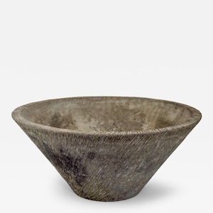 May include: A large, conical bowl with a weathered, grey stone-like texture. The exterior surface features fine, diagonal etched lines radiating from the base to the wide, circular rim, creating a rough, organic appearance with dark patches.