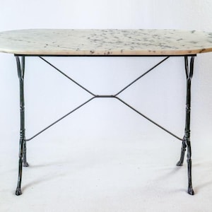 May include: An oval table featuring a white marble top with grey veining and a black metal base. The base consists of four slender legs connected by a central X-shaped support structure, providing a stable foundation for the stone surface.