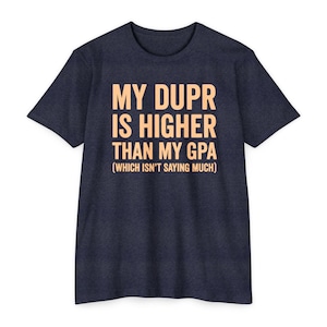 May include: A dark navy blue short-sleeved t-shirt featuring the light peach-coloured text MY DUPR IS HIGHER THAN MY GPA (WHICH ISN'T SAYING MUCH) printed in a bold, sans-serif font across the centre of the chest area of the garment.
