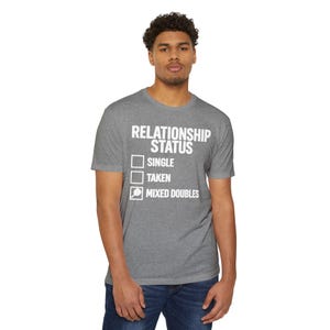 Op de afbeelding: Een grijs gem&ecirc;leerd T-shirt met korte mouwen en de witte tekst RELATIONSHIP STATUS, gevolgd door een checklist met de opties SINGLE, TAKEN en MIXED DOUBLES, met een kleine afbeelding van een pickleball-racket in het laatste selectievakje.