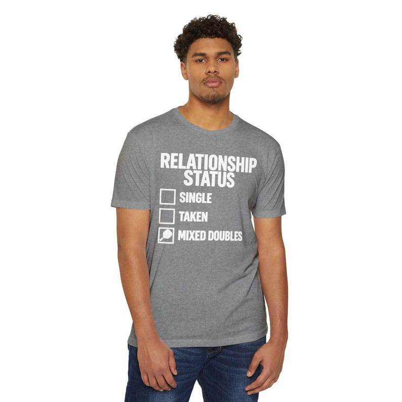 Op de afbeelding: Een grijs gem&ecirc;leerd T-shirt met korte mouwen en de witte tekst RELATIONSHIP STATUS, gevolgd door een checklist met de opties SINGLE, TAKEN en MIXED DOUBLES, met een kleine afbeelding van een pickleball-racket in het laatste selectievakje.