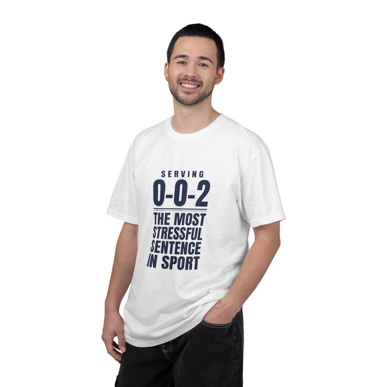 May include: A white short-sleeved t-shirt featuring dark blue text that reads "SERVING 0-0-2 THE MOST STRESSFUL SENTENCE IN SPORT" centered on the chest. The garment has a crew neckline and a standard fit, constructed from a plain white fabric.