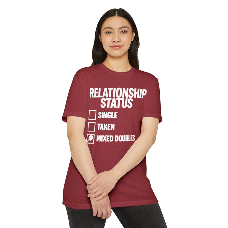 Op de afbeelding: Een bordeauxrood t-shirt met korte mouwen en witte tekst met de tekst RELATIONSHIP STATUS gevolgd door drie selectievakjes. De eerste twee zijn leeg, terwijl het derde vakje is aangevinkt en is gelabeld met MIXED DOUBLES en een pickleball-icoon.