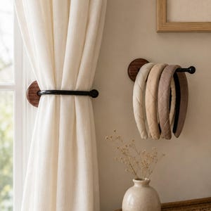 May include: A wall-mounted organizer featuring a dark wood circular base and a black metal rod. The rod holds four padded headbands in neutral shades of cream, beige, tan, and brown, each with a quilted texture and a black interior lining.
