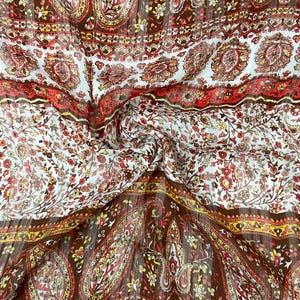 May include: A lightweight fabric featuring a repeating paisley and floral pattern in shades of brown, red, orange, and yellow on a white background. The material has a subtle vertical ribbed texture and is arranged in horizontal bands.