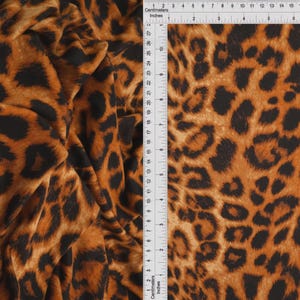 May include: Fabric featuring a brown and black leopard print pattern. A white ruler is positioned along the top and side, showing measurements in both inches and centimeters, with the fabric width extending past 8 inches and 20 centimeters.