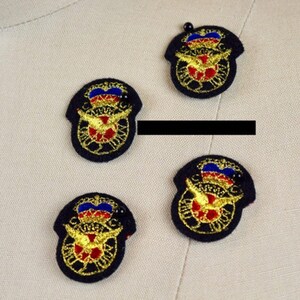 May include: Four circular embroidered patches featuring a central red and gold emblem with wings, topped by a blue and red crown design. Each patch is outlined in black thread and includes a small black bead accent at the top of the crown.