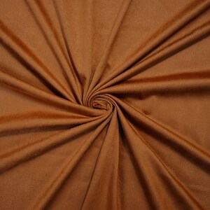 May include: A solid, medium-brown fabric with a soft, matte texture. The material is gathered in the center, creating deep, radiating folds and shadows that emphasize the smooth, consistent color and the fine, uniform surface of the textile.