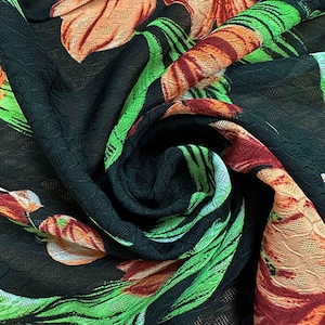 May include: A black fabric featuring a vibrant floral pattern with large orange and red blossoms accented by bright green leaves. The material has a textured, slightly sheer, and crinkled surface with a repeating grid-like weave throughout the cloth.