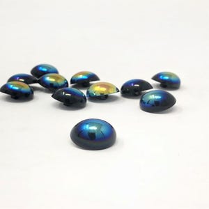 May include: A collection of eleven small, dome-shaped buttons with a smooth, iridescent finish. Each button displays a shifting color gradient that transitions from deep navy blue to vibrant metallic gold and green tones across the surface.
