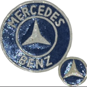 May include: Two circular patches featuring the Mercedes-Benz logo. The larger patch displays the text MERCEDES BENZ in silver sequins against a dark blue sequined background, with a central three-pointed star. A smaller matching patch is included.