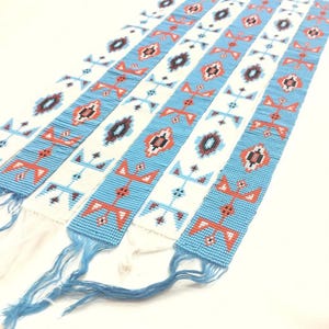 May include: A series of long, narrow beaded strips featuring alternating vertical bands of light blue and white. The strips are decorated with geometric patterns in shades of orange, dark brown, and black, and each end terminates in loose thread fringe.