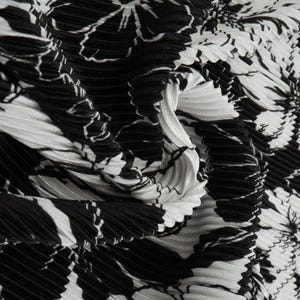 May include: A pleated fabric featuring a high-contrast black and white floral pattern. The material has a distinct accordion-style texture with deep folds and ridges that create a dynamic, rippled surface across the entire textile design.