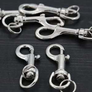 May include: A collection of silver-toned metal lobster claw clasps with swivel bases and attached split rings. The hardware features a polished, reflective finish with a spring-loaded gate mechanism for secure attachment to various items.