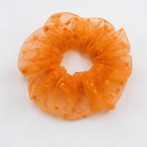 May include: A bright orange hair scrunchie made of a sheer, mesh-like fabric featuring a delicate dotted pattern throughout. The accessory has a gathered, ruffled texture that creates a voluminous, circular shape with a central opening.