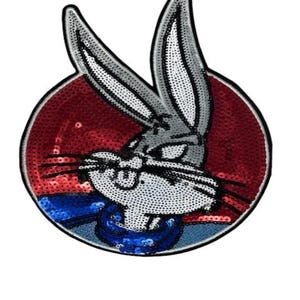 May include: A circular embroidered patch featuring a sequined Bugs Bunny character. The rabbit has grey ears and a white face with black whiskers. The background is a vibrant red, and the character wears a blue collar, all outlined in black.