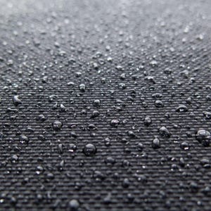 May include: A close-up view of a black, woven fabric surface covered in numerous clear water droplets. The texture of the material is visible beneath the beads of moisture, which vary in size and are scattered across the dark, grid-like pattern.