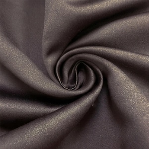 May include: A dark charcoal gray fabric featuring a subtle metallic gold shimmer throughout the material. The textile is gathered into a central swirl, creating deep folds and shadows that highlight the reflective quality of the fabric surface.