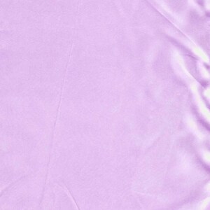 May include: A solid light lavender fabric with a smooth, satin-like finish. The material features a soft sheen and gentle, flowing folds that create subtle highlights and shadows across the surface, emphasizing the uniform color and texture.