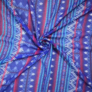 May include: A lightweight fabric featuring a vibrant geometric pattern in shades of royal blue, bright red, turquoise, and white. The design consists of repeating vertical stripes, zigzag lines, and diamond shapes arranged in a symmetrical layout.