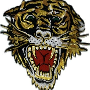 May include: A tiger head patch featuring gold, black, and white sequins with a red embroidered mouth. The design shows a snarling tiger with green eyes, white whiskers, and sharp teeth, crafted with detailed stitching and reflective sequin accents.