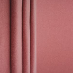 May include: A solid dusty rose colored fabric with a soft, matte, and slightly fuzzy texture. The material is displayed with three vertical folds running down the left side, creating subtle shadows and depth across the uniform textile surface.
