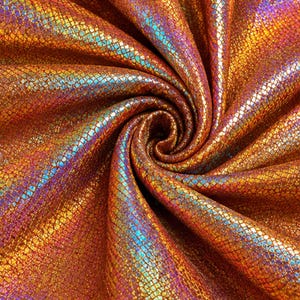 May include: A metallic fabric featuring a repeating hexagonal scale pattern in shades of copper, bronze, and gold. The material is arranged in a tight spiral, creating deep folds and shadows that highlight the iridescent blue and purple highlights.