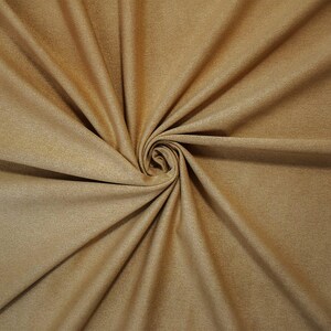 May include: A solid tan fabric with a soft, matte, suede-like texture. The material is gathered into a central spiral, creating deep, radiating folds and shadows that highlight the consistent light brown color and the fine, uniform grain of the textile.