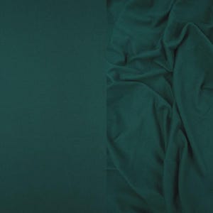 May include: A solid dark teal fabric shown in two states: a smooth, flat section on the left and a draped, folded section on the right. The material has a matte finish and a consistent deep green-blue color throughout the entire surface area.