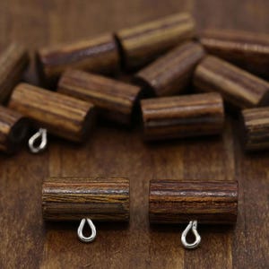 May include: A collection of cylindrical wooden beads featuring a dark brown wood grain pattern. Each bead is horizontally oriented and includes a small, silver-toned metal loop attached to the bottom, designed for hanging or connecting components.