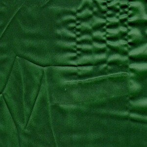 May include: A deep forest green fabric featuring a smooth, matte texture with subtle, irregular folds and creases. The material displays a series of vertical, parallel stitched lines that create a quilted or pleated effect across the surface.