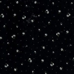 May include: A black fabric featuring a repeating pattern of small white flowers and tiny white dots scattered across the surface. The floral design consists of simple four-petaled blossoms arranged in a consistent, evenly spaced layout throughout.