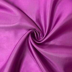 May include: A vibrant magenta fabric with a smooth, lustrous finish. The material is gathered into a central swirl, creating deep, flowing folds and shadows that highlight the reflective quality and consistent, solid color of the textile surface.