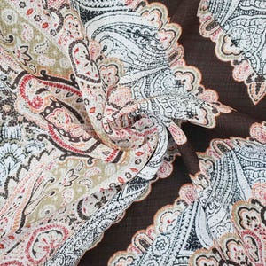 May include: A fabric textile featuring a detailed paisley pattern in shades of dark brown, cream, black, and muted orange. The intricate design consists of swirling teardrop shapes and floral motifs printed across the surface of the woven material.