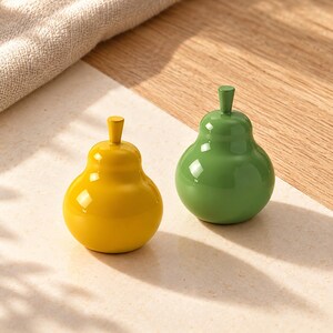 May include: Two pear-shaped decorative objects with a smooth, glossy finish. One object is bright yellow and the other is a solid medium green. Both items feature a small, upright stem at the top and a rounded, bulbous base design.