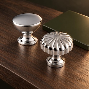 May include: Two polished silver-toned metal cabinet knobs. One knob features a smooth, rounded, dome-shaped top, while the other knob has a textured, fluted, radial design with multiple vertical ridges radiating from the center to the edge.