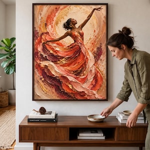May include: A framed wall art print featuring an oil painting of a dancer in a flowing, textured dress of red, orange, and gold hues. The figure is captured in a dynamic pose with one arm extended upward against a circular, sun-like background.