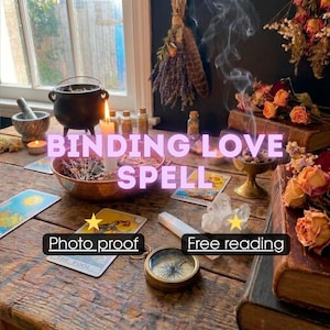 May include: A wooden table displays a black cauldron, a lit white candle, and a bowl containing dried herbs. Tarot cards, including The Fool, are spread out alongside a brass compass, a clear crystal, and dried flowers. Text reads BINDING LOVE SPELL, Photo proof, and Free reading.
