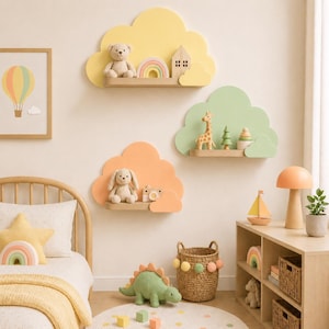 Op de afbeelding: Drie wolkvormige wandplanken in pastelgeel, lichtgroen en zacht oranje. Elke plank heeft een platte houten basis voor het uitstallen van klein speelgoed, waaronder een teddybeer, een houten huisje, een giraffefiguur en een camera.