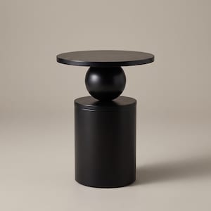 May include: A matte black side table featuring a circular tabletop supported by a central spherical element resting on a cylindrical base. The structure is composed of three distinct geometric shapes stacked vertically in a solid black finish.