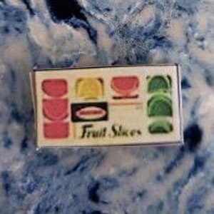 May include: A vintage box of Fruit Slices candy. The box is white with a red, yellow, and green design. The box says "Fruit Slices" in black letters.