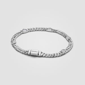 May include: A silver chain link bracelet featuring a series of evenly spaced heart-shaped clear stones set within the links. The bracelet includes a rectangular clasp engraved with the word PANDORA, providing a secure closure for the piece.
