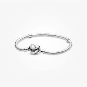 May include: A silver snake chain bracelet featuring a heart-shaped clasp. The clasp is engraved with the text PANDORA and has a polished metallic finish. The bracelet consists of a flexible, textured chain with two fixed stations for charms.