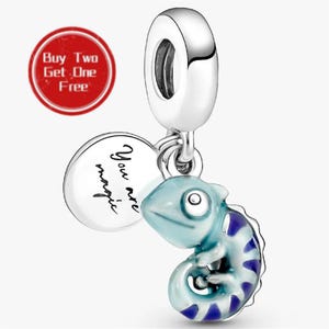 Puede incluir: Un charm de plata con forma de camaleón en azul claro y oscuro con la cola enroscada. Incluye un disco redondo de plata grabado con el texto You are magic. El charm cuenta con una anilla cilíndrica en la parte superior para su sujeción.