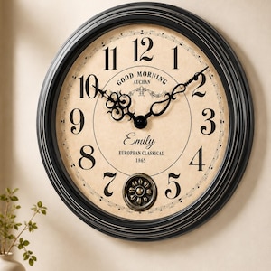 Puede incluir: Un reloj de pared redondo con marco negro y esfera beige con números arábigos negros. El centro muestra el texto GOOD MORNING AUCHAN, el nombre Emily y las palabras EUROPEAN CLASSICAL 1865. Tiene manecillas negras ornamentadas y un medallón.