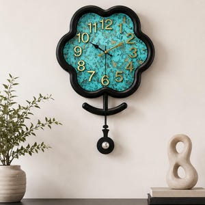 Peut inclure: Une horloge murale en forme de fleur avec un cadre noir et un cadran marbré turquoise et doré. Elle présente des chiffres arabes dorés en relief, des aiguilles noires pour les heures et minutes, une trotteuse dorée et un balancier noir.