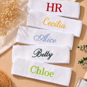 May include: Five white waffle-textured fabric headbands arranged in a vertical stack. Each headband features custom embroidery in different colors: red text HR, yellow script Cecilia, light blue script Alice, dark green script Betty, and lime green Chloe.